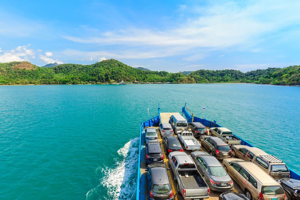 Image related to blog title Cars loaded on a ferry crossing a scenic bay, representing car shipping challenges
