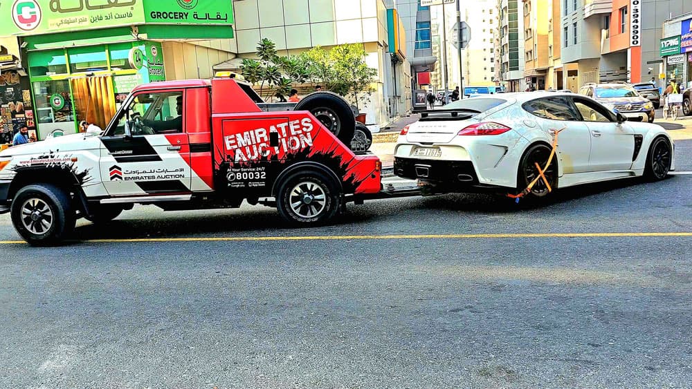 Image related to blog title Truck towing a luxury car for auction car transport service in a busy city street with clear branding.