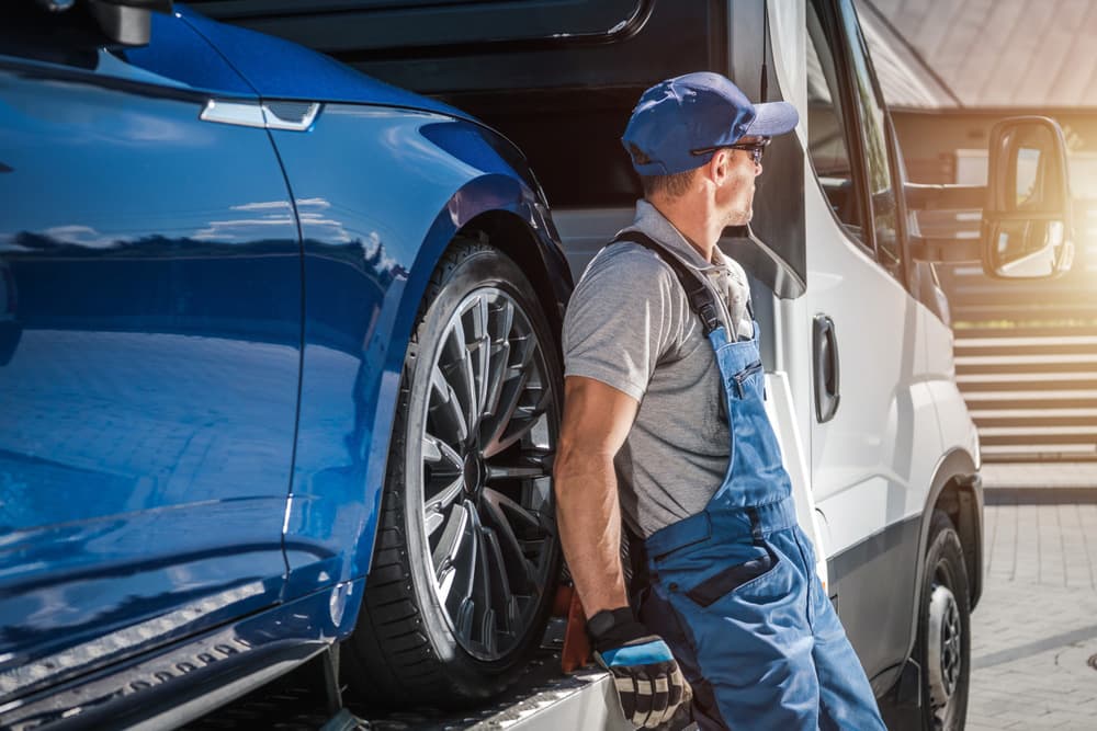 Image related to blog title Auto transport driver preparing to ship a car securely on a transport truck under sunny conditions.