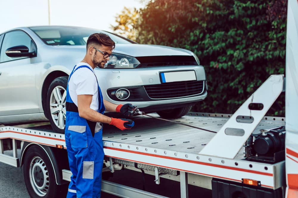 Image related to blog title Mechanic securing a car onto a trailer for transport, illustrating DIY vs. Professional Car Transport options.