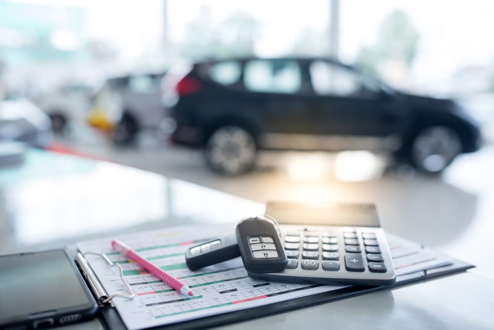 Image related to blog title Calculator, car keys, and documents on a table with a blurred car in the background for shipping a financed car.