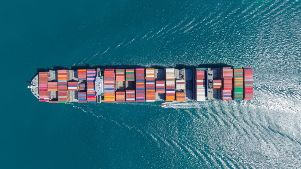Image related to blog title Aerial view of a cargo ship carrying colorful containers across the sea, symbolizing contingent cargo insurance.