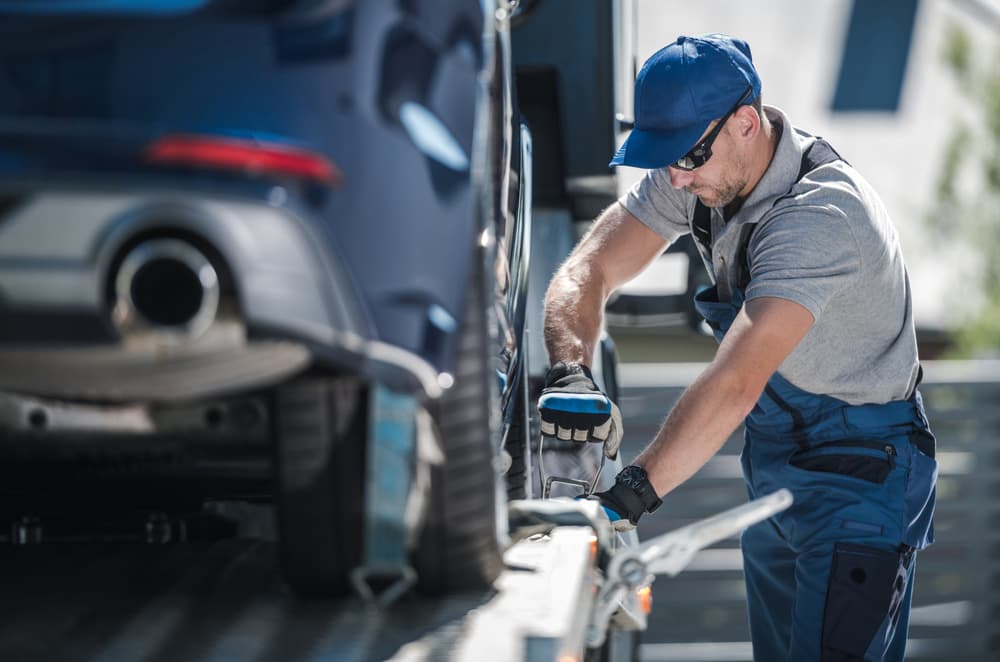 Image related to blog title Auto shipping company worker securing a car on a transport trailer for safe delivery to its destination.